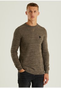 Brauner Strickpullover mit langen Ärmeln und Rundhalsausschnitt, ausgestattet mit einem kleinen Logo auf der Brust und einer strukturierten Oberfläche.