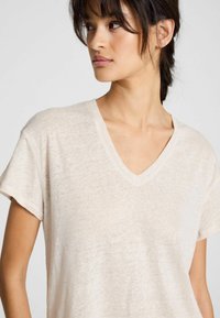 T-shirt a V in beige chiaro, realizzato in un materiale morbido e strutturato, con maniche corte e una vestibilità rilassata, che mette in risalto uno stile informale.