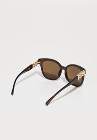 Braune Schildpatt-Sonnenbrille mit dunklen Gläsern, rechteckiger Form und dekorativen Akzenten in goldener Farbe an den Schläfen. Glänzende Oberfläche der Fassung.