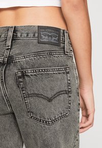 Primer plano de una persona que lleva puesta una jeans de mezclilla gris de tiro alto con una etiqueta de Levi Strauss & Co. encima del bolsillo trasero.