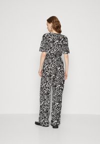 Combinaison à motifs floraux noir et blanc avec des manches courtes, une coupe décontractée et des jambes larges. Tissu lisse avec un détail de taille cintrée.
