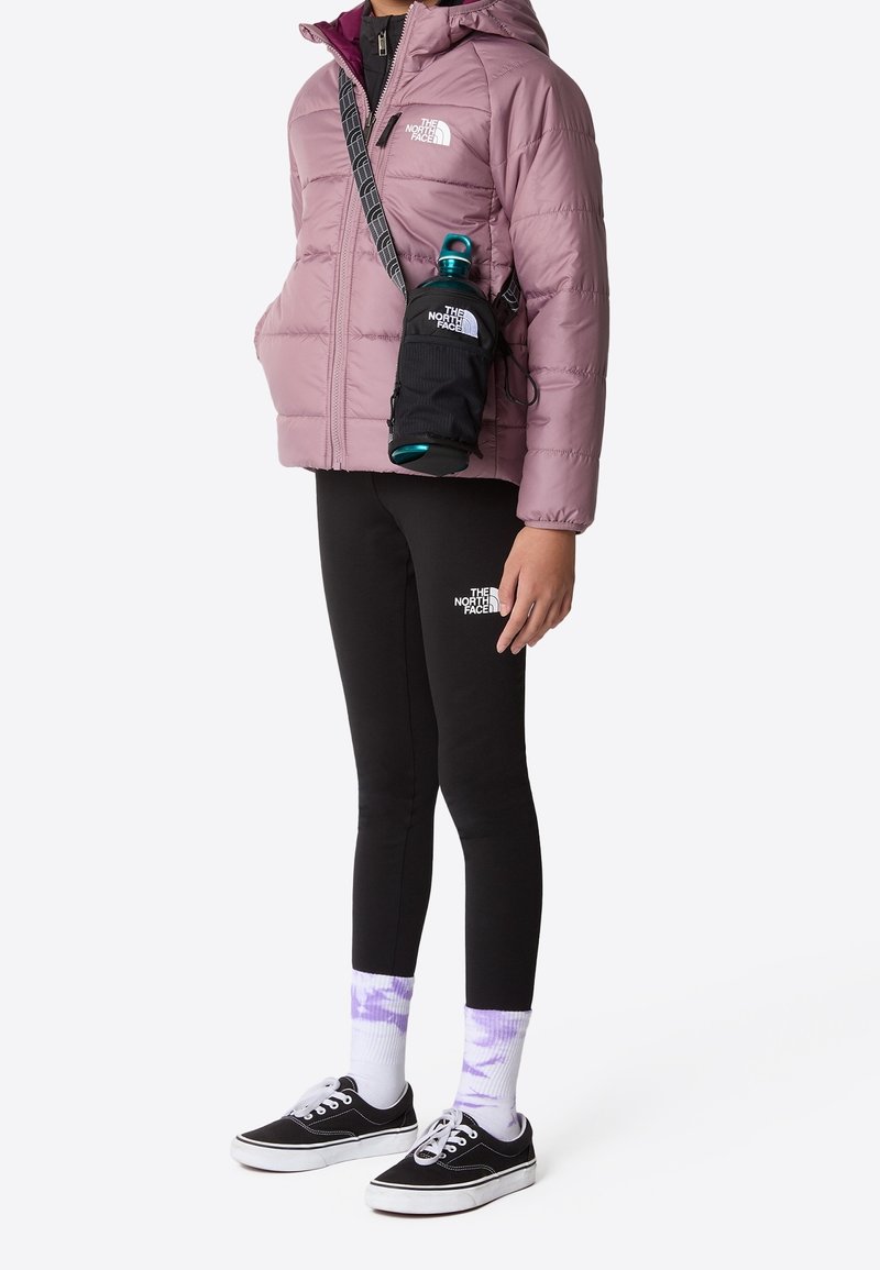 Osoba nosząca mauve'ową kurtkę puchową, czarne legginsy, czarną torbę na ramię trzymającą butelkę wody, fioletowe skarpetki w tie-dye oraz czarne sneakersy.