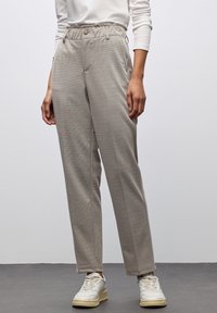 Ljusgrå, strukturerade byxor med resårmidja, framfickor och en avslappnad passform. Kombineras med vita sneakers.