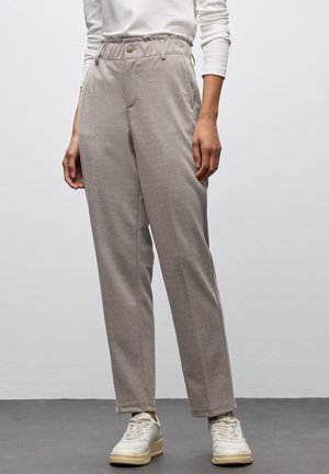 Helle graue, strukturierte Hose mit elastischem Bund, Seitentaschen und lockerer Passform. Kombiniert mit weißen Sneakers.