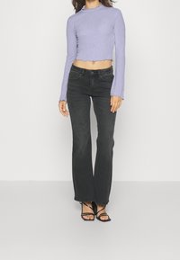 Kvinde iført en lavendelfarvet langærmet cropped top, sorte højtaljede bootcut-jeans og sorte hælede sandaler med stropper.