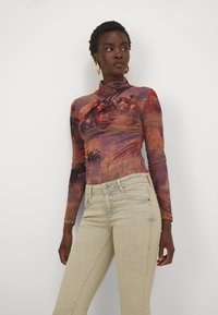 Haut à manches longues en imprimé abstrait multicolore avec un design ajusté et un col montant, associé à un jean skinny de couleur claire. Texture de tissu lisse.