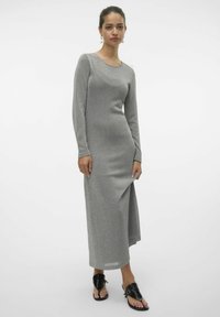 Långärmad grå klänning i stretchigt, glittrande tyg. Har en rundad halsringning och sidoklyfta, kombinerad med svarta platta sandaler.