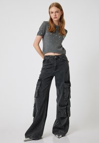 Grijze gebreide crop top met parel details, gecombineerd met hoge zwarte cargobroeken met zijzakken en een losse pasvorm. Zilveren schoenen accentueren.