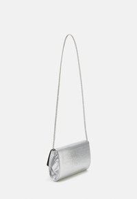 Piccola borsa crossbody argentata con texture, dotata di una lunga e sottile tracolla che pende su uno sfondo bianco.
