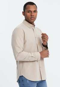 Beige overhemd met lange mouwen, met een button-down kraag, subtiele textuur, slim fit, gebogen zoom en met knopen sluitende manchetten, gedragen met blauwe jeans.