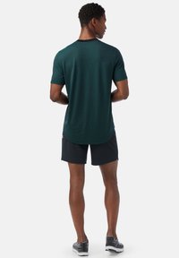 Grönrandig sporttröja med rundad nederkant, korta ärmar och svarta detaljer, ihop med svarta shorts och mönstrade löparskor.