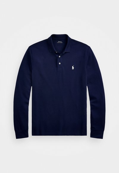 Jūras zila krekla polo ar garām piedurknēm, izgatavota no kokvilnas. Tam ir klasiskā apkakle, divu pogu aizdare un neliels izšūts logo uz krūtīm.