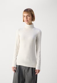 Cream-colored long-sleeve turtleneck top made of soft fabric, featuring a slim fit and a minimalistic design. Paired with gray, pleated pants.