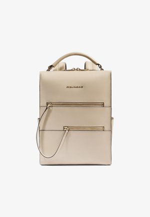 Mochila de cuero beige con herrajes dorados, que cuenta con un asa superior, correas ajustables y dos bolsillos frontales con cremallera. Textura lisa.