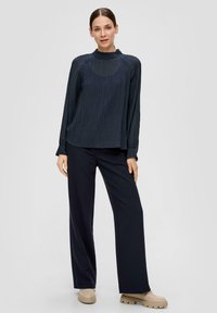 Marineblauwe lange mouw top van textuurstof met hoge hals, gecombineerd met marineblauwe wijde broek en beige schoenen met dikke zool.
