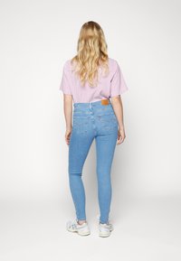 Jeans azul claro de tiro alto con un ajuste slim y dos bolsillos traseros, combinados con una camisa de cuadros vichy rosa y blanca.