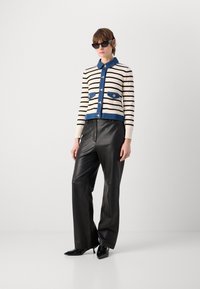 Cardigan a righe in crema e nero con dettagli in denim, dotato di colletto e doppie tasche frontali. Abbinato a pantaloni in pelle nera e tacchi.
