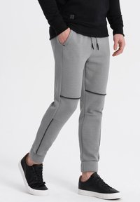 Graue Jogginghosen mit gerippten Seiteneinsätzen, elastischem Bund und schwarzen Akzenten, kombiniert mit schwarzen Sneakern mit weißer Sohle.