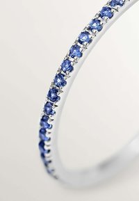 Brazalete de plata con una fila de piedras preciosas azules engastadas en lugares prisioneros, con una superficie suave y pulida y un diseño circular delgado.
