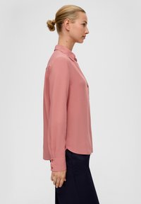 Rosa langärmlige Bluse mit Kragen und Knopfakzenten. Glatter Stoff mit einer leicht lockeren Passform, kombiniert mit dunklen Hosen.