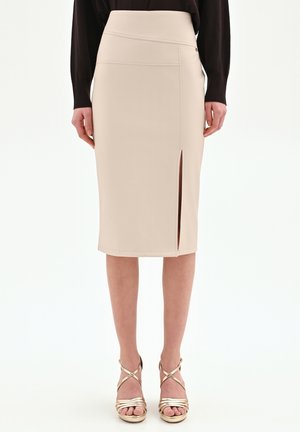 Gonna beige a tubino al ginocchio con spacco frontale indossata con sandali con tacco alto dorati metallici e top nero.