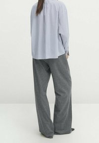 Chemise oversize à rayures bleues et blanches associée à un pantalon large gris, mettant en avant une coupe décontractée et des textures douces.