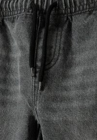 Grå denimjoggers med en texturerad tyg, utrustade med en svart dragsko med metalländar och elastisk midja. Inga synliga fickor.