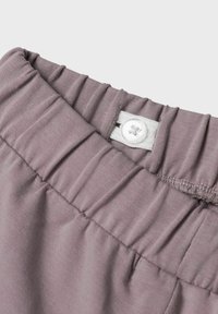 Gaiši violets audums, savilkta josta ar elastīgu un baltu pogu detaļu. Gluda tekstūra ar smalkiem krokiem, kas uzlabo dizainu.