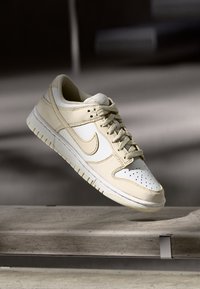 Beige Leder-Sneaker mit einer perforierten weißen Zehenbox, Schnürdesign und strukturierten Akzenten. Verfügt über eine Gummisohle.