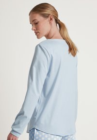 Lichtblauw lange mouwen top gemaakt van zachte stof. Heeft een ronde halslijn en een afgeronde zoom, gecombineerd met polka dot pyjamabroek.