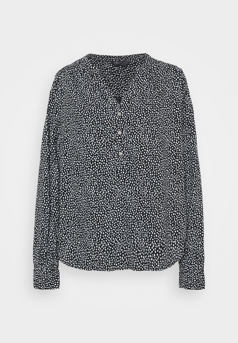 Blouse noire à manches longues avec motif à pois blancs, boutonnée à l'avant et col en V, présentée sur fond blanc uni.