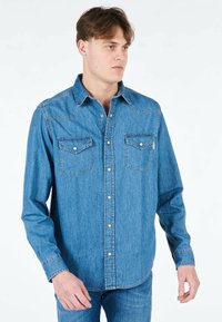Camicia di jeans in azzurro chiaro con chiusura a bottoni, colletto a punta, due tasche sul petto e cuciture in contrasto lungo le cuciture.