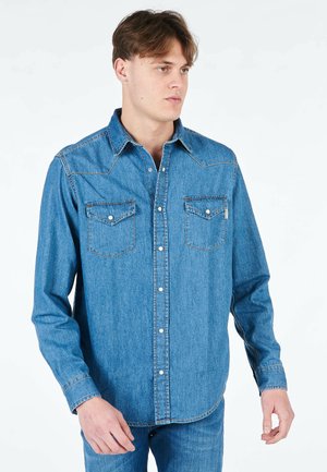 Camicia di jeans in azzurro chiaro con chiusura a bottoni, colletto a punta, due tasche sul petto e cuciture in contrasto lungo le cuciture.