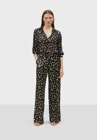 Black sheer blouse with beige polka dots, buttoned front, rolled sleeves, paired with matching wide-leg trousers, featuring a similar pattern.