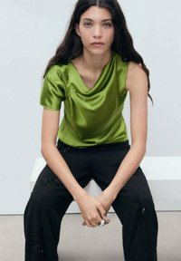 Top en satin vert avec un décolleté drapé, associé à un pantalon noir orné de délicates broderies florales. Design simple et moderne.