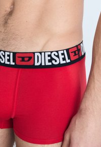 Raudoni vyriški bokseriai su juodu juosmeniu, ant kurio užrašyta baltais rašmenimis "DIESEL". Medžiaga glotni, pasižyminti elegantišku ir prigludusiu dizainu.