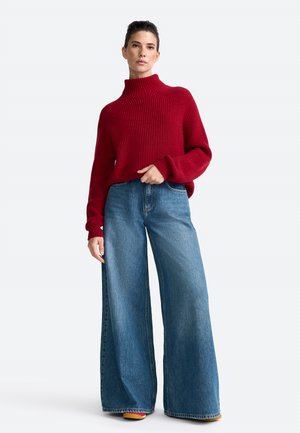 Rode geribbelde trui met hoge hals, gecombineerd met wijduitlopende blauwe denim broek. De outfit heeft een relaxte pasvorm en een gestructureerd breiwerk ontwerp.