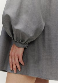 Graues Kleid mit Puffärmeln und gerafften Bündchen. Glatter, strukturierter Stoff mit subtiler Schimmer, der ein einfaches, lockeres Design präsentiert.