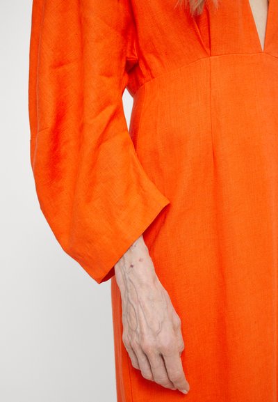 Orange linen dress with a deep V-neck and wide, billowing sleeves. Features a textured fabric and clean, structured lines.