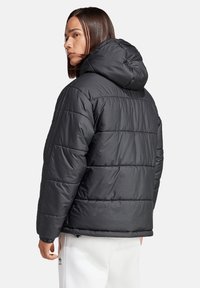 Zwarte pufferjack met capuchon, voorzien van gestikte secties, elastische manchetten en een gladde textuur. Minimalistisch ontwerp zonder zichtbare logo's.