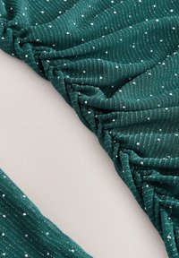 Tyrkisblåt tekstureret stof med opsamlede områder og små, blanke sølvprikker jævnt fordelt over det hele. Glat finish og blød fald.