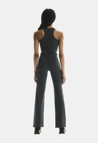 Crni prugasti crop top i uske hlače s raširenim nogavicama, izrađeni od teksturiranog materijala, s neprekidnim dizajnom bez vidljivih hardverskih detalja.