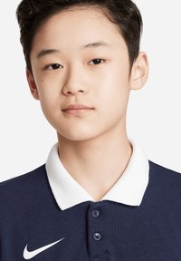 Marineblauwe polo met witte kraag, voorzien van drie knopen en een Nike-logo. Gladde stoftextuur, ontworpen voor casual gebruik.