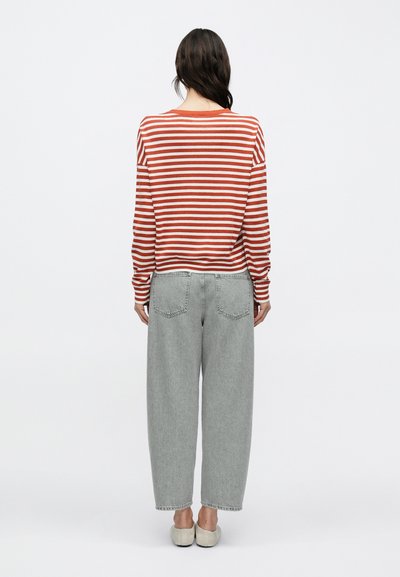 Κόκκινο και άσπρο ριγέ πουκάμισο με μακριά μανίκια, συνδυασμένο με ανοιχτό γκρι, φαρδιά τζιν παντελόνια και μπεζ παπούτσια. Casual πλάγια όψη.