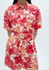 Sukienka koszulowa w kolorze białym z czerwonymi i pomarańczowymi wzorami kwiatowymi, z krótkim rękawem, guzikami z przodu oraz szerokim paskiem z okrągłą klamrą.