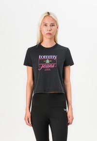 Černé zkrácené tričko s kulatým výstřihem. Obsahuje barevné logo "tommy jeans" a text "1985". Měkká bavlněná tkanina, krátké rukávy.