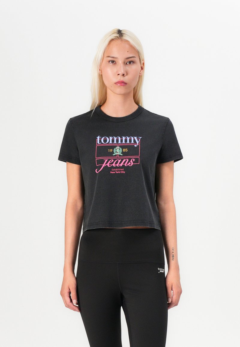 Černé zkrácené tričko s kulatým výstřihem. Obsahuje barevné logo "tommy jeans" a text "1985". Měkká bavlněná tkanina, krátké rukávy.