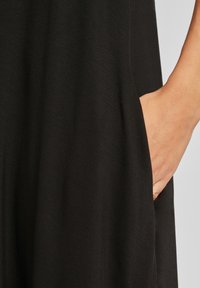 Vestito nero con una tasca laterale, realizzato in un tessuto morbido e liscio con una texture fluida e una vestibilità comoda.