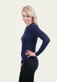 Pull bleu marine à manches longues avec un col rond, de forme ajustée et texture lisse, accompagné de pantalons noirs.