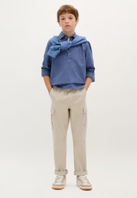 Blaues Langarmhemd mit Kragen, beige Cargo-Hosen und Sneakern. Pullover um den Hals gebunden. Taschen an den Hosen, lässiges Design.